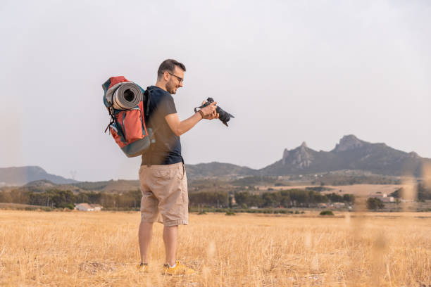 istock Photographer looking at his camera with a smiling expression, in a meadow, with a mountaineer's backpack. Horizontal photography, with copy space. 1405594420