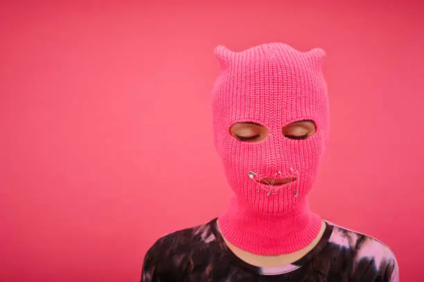 Portrait of yung girl in pink balaclava with closed mouth and eyes having no rights isolated on p