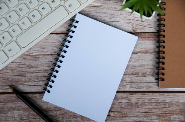 istock Top view of simple office desk with computer keyboard, pen and blank notepad. 1405595449