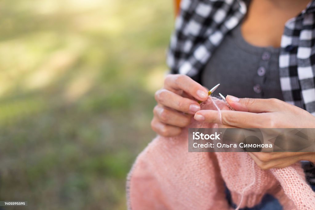 A woman's hands are knitting a woolen cloth from a ball of pink threads. Clothes with their own hands, needlework. Knitting Needle Stock Photo
