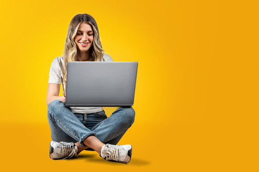 Smiling beautiful woman sitting on the floor is using laptop