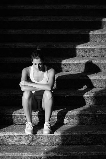 Tired sporty woman sitting on stairs for resting after outdoor urban running and fitness workout.