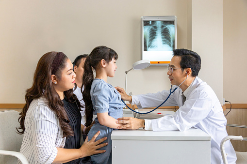 Asian doctor is diagnosis young girl using stethoscope for lung checkup and side effect on coronavirus with parent and family in her appointment in hospital