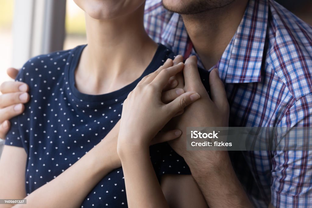 Close up shot of young couple hugging at window Close up shot of young couple hugging at window. Husband embracing wife from behind, holding, touching shoulders, giving love, care, comfort, support. Marriage, relationship concept Miscarriage Stock Photo