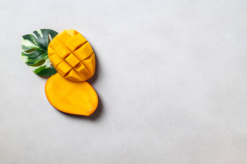 Mango background design concept. Top view of diced fresh mango fruit pattern with leaves on gray table.