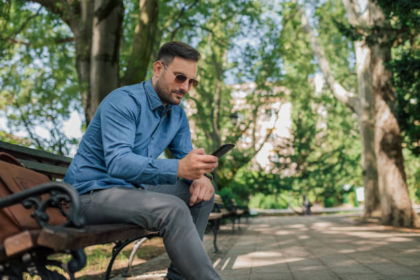 istock Business professional messaging on smart phone while sitting on bench at park 1405602592