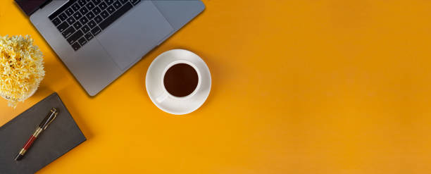 istock Top view yellow office desk with laptop, notebook and coffee cup background. Panoramic banner template 1405603859