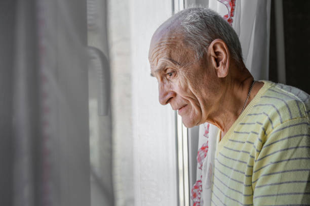 istock Lonely granddad looking through window glass standing at home 1405604324