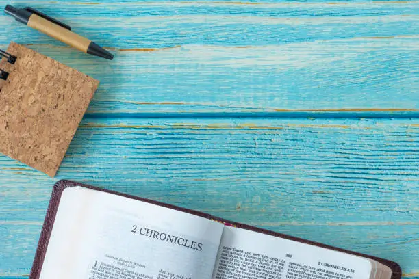 2 Chronicles open Holy Bible Book, notebook, and pen on a rustic wooden background with copy space. Top table view. Flat lay. Studying Old Testament Scriptures. Christian biblical concept. A close-up.