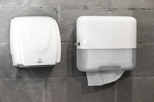 Paper towel dispenser and hand dryer on concrete wall on modern stylish bathroom in loft style