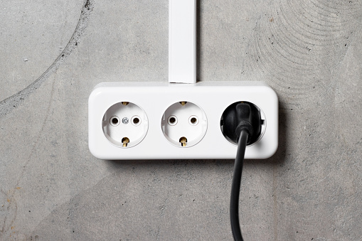 Group of white european electrical outlets with plug on gray concrete wall