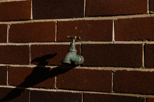 Section of an old dark brown brick wall with a brass tap.