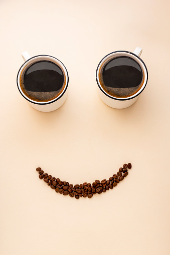 Smile face made from two cups of coffee and coffee beans. Cute, fun coffee mockup. Morning positive coffee concepts