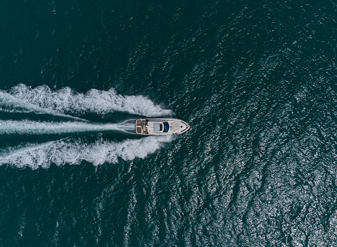 Aerial top down view of white speed motor boat on open sea at summer day