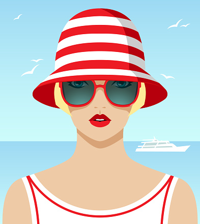 Beautiful blonde woman on vacation wearing large fashionable red sunglasses, striped hat and white t-shirt in front of ocean with yacht and blue sky with flying birds