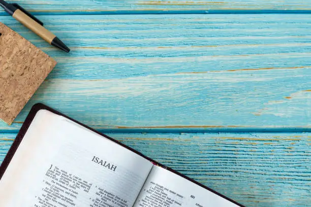 Photo of Isaiah open Holy Bible Book on a rustic wooden background with a notebook and pen