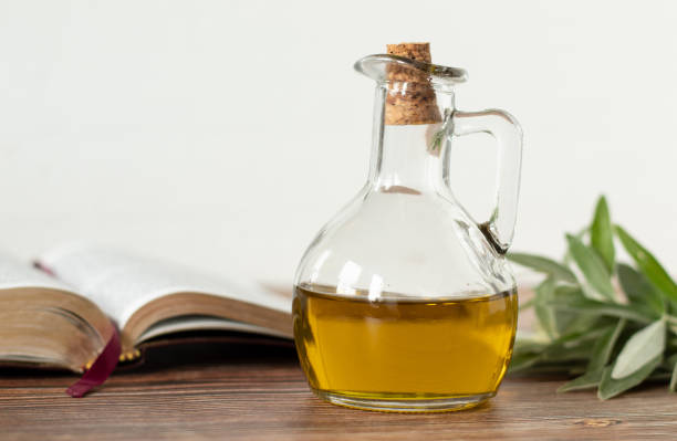 aceite de oliva puro en un frasco de vidrio, un libro bíblico abierto y una rama de olivo verde en una mesa de madera con fondo blanco - consecrated fotografías e imágenes de stock