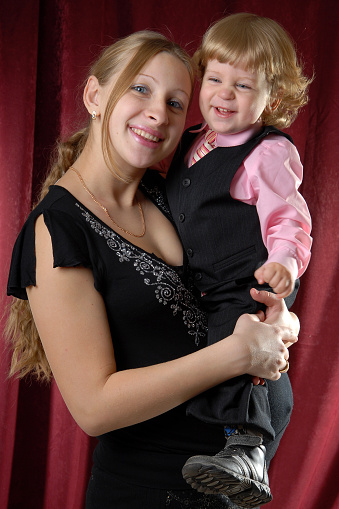 A beautiful girl in a black blouse holds in her arms a blond-haired. blue-eyed boy in a pink shirt