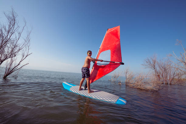 windsurfer débutant garçon planche à voile sur la plage du lac. - child nautical vessel summer swimming goggles photos et images de collection