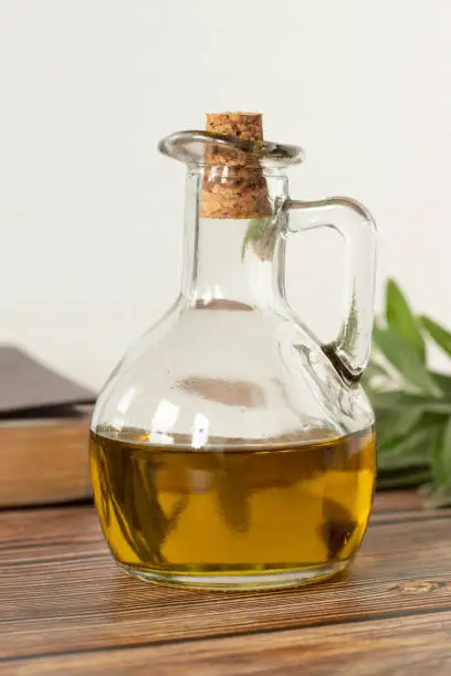 Pure olive oil in a glass jar, a closed Bible Book, and a green olive branch on a wooden table with white background. Symbol of God's Holy Spirit. Christian biblical concept. Vertical shot. Close-up.