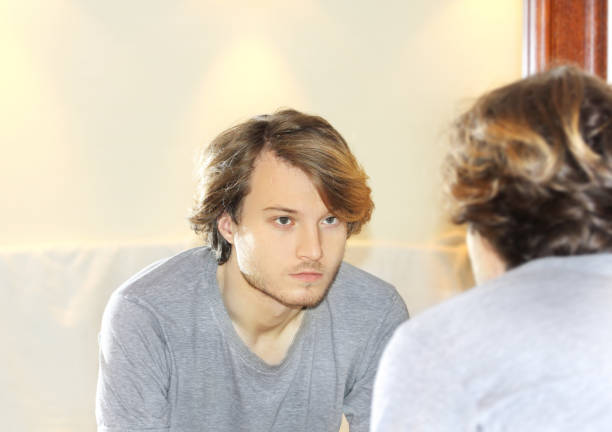 istock young man looking in the mirror,combing his hair,looking at problems on face 1405621806
