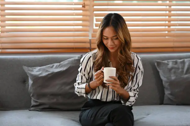 Portrait of smiling curly-hair girl holding a cup of coffee, sitting in the living room, Business and financial concepts.