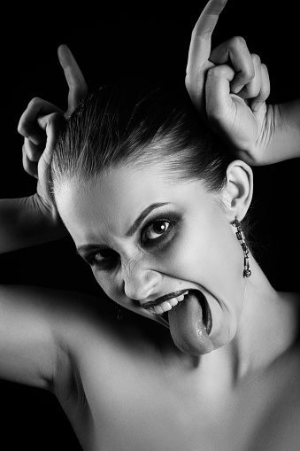 fun luxury woman show horns and tongue on black background, looking at camera, monochrome