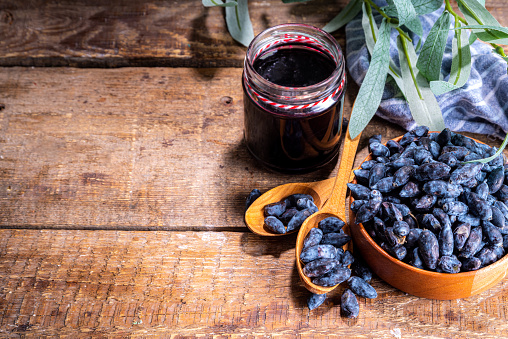 Small glass jar with homemade  haskap berry jam, on wooden background with bowl of fresh haskap (honeysuckle, honeyberry) berries, copy space