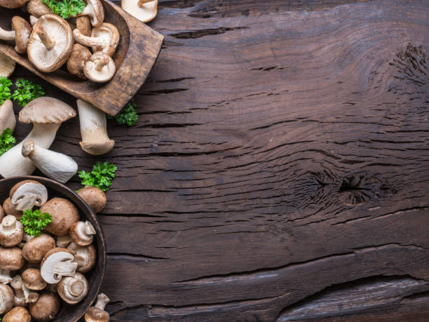 istock Different brown colored edible mushrooms on wooden table with herbs. Top view. 1405627520