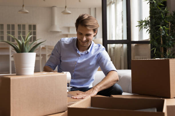 istock Smiling young man packing belongings in carton boxes. 1405627810