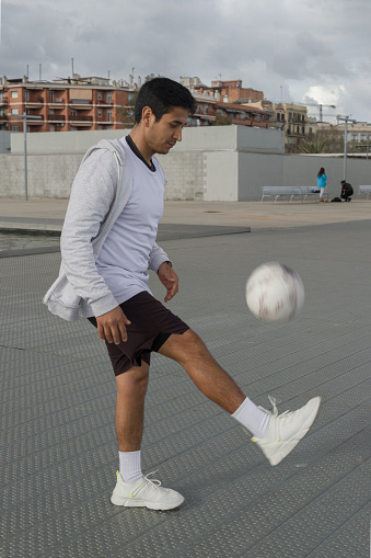 full length | side view of a peruvian-feature man dominating the soccer ball with foots in a public place