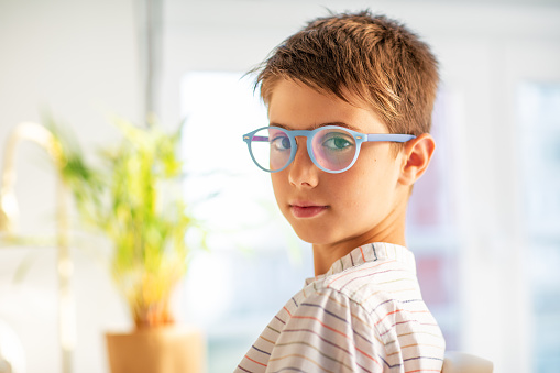 Emotional portrait of a boy looking straight at the camera wearing blue frame glasses.