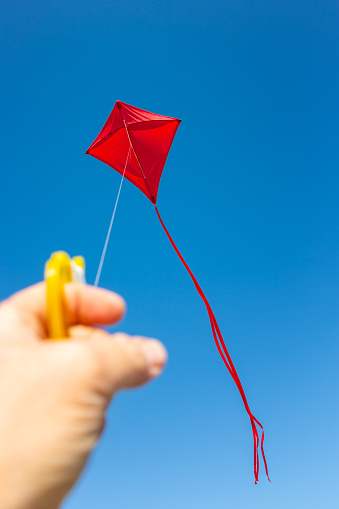 Hand holding red kite on string. Focus on kite, shallow DOF.
