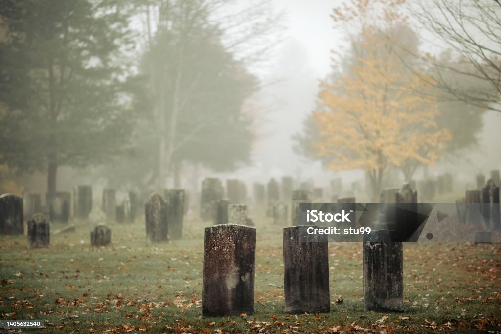 Three gravestones standing in a foggy graveyard during the fall Three gravestones standing in a foggy graveyard during the fall. Focus is on front headstone. Cemetery Stock Photo