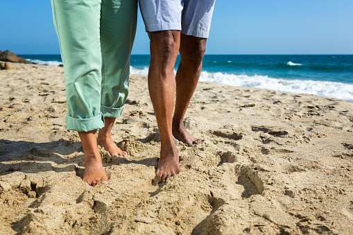 Legs of senior African American couple walking with at sandy beach. Model released.