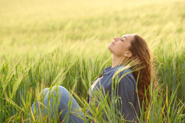 femme assise dans un champ de blé respirant de l’air frais - exercice de respiration photos et images de collection