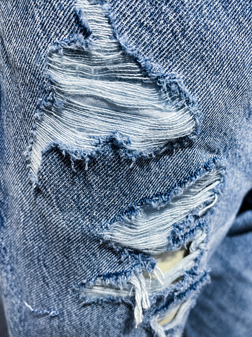 Stock photo showing close-up view of a pair of pre-ripped blue denim jeans sporting frayed holes.