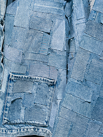 Stock photo showing close-up, elevated view of a pair of blue denim jeans sporting a customised design of bleached patches of fabric swatches.