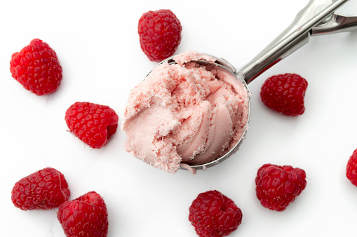 Refreshing cold sweets, seasonal dessert and cool summertime treat concept with close up on scoop of vivid pink raspberry ice cream and scattered raspberries isolated on white marble background