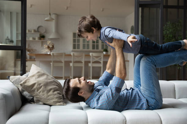 istock Happy young father lying on couch, lifting excited son 1405636315