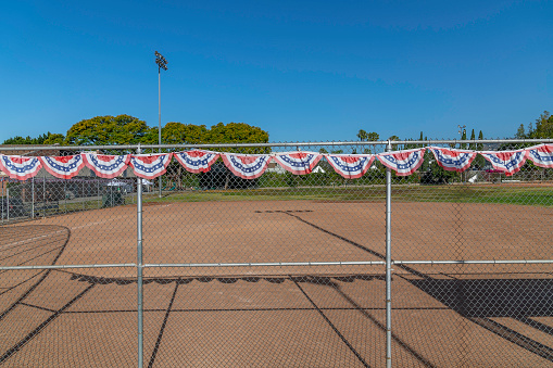 American flag bunting tied to a chain link fence surrounding a baseball field.