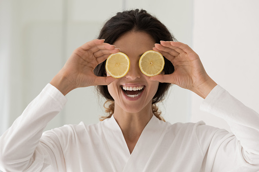 Happy young smiling woman in bathrobe holding lemon slices, feeling excited of natural cosmetics spa procedures or vitamin C skincare results, recommending organic ingredients in dermatology treatment