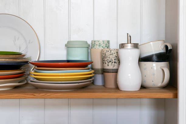 istock Wooden shelf with kitchen utensils, rustic style. Tableware, plates and cups stand on a shelf in the kitchen. Cupboard with set of colourful dishes, modern interior. 1405641662
