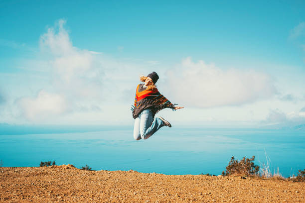 Woman Jumps Over Sandstone Boulders against blue sky