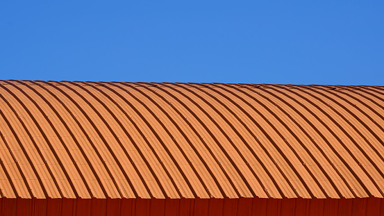 Curve line pattern of orange corrugated steel curved roof against blue clear sky background