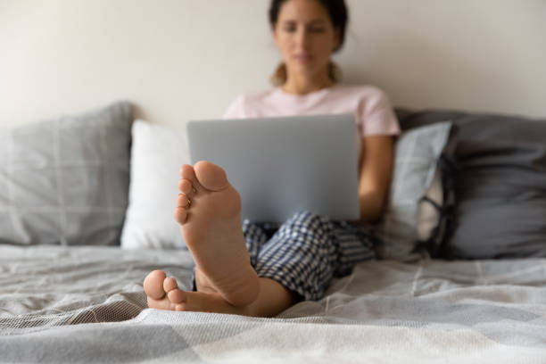 jeune femme latine se détendre pieds nus avec un ordinateur portable sur un lit confortable - mid adult women human skin neat good condition photos et images de collection