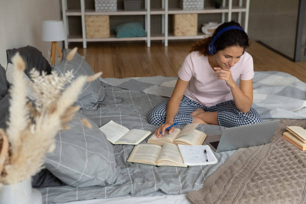 istock Young female in headphones study using books laptop on bed 1405644533