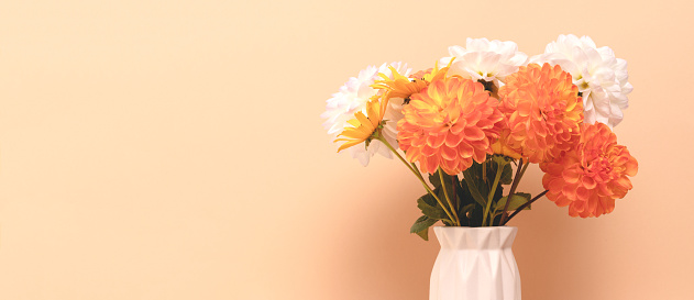 Banner with bouquet of dahlia flowers in vase in front of beige background. Floral springtime composition with copyspace.