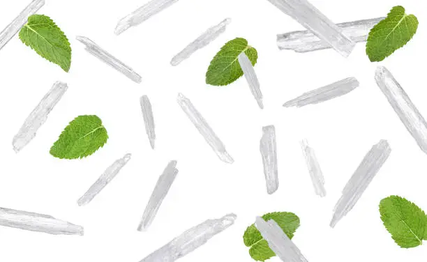 Translucent menthol crystals and green mint leaves falling on white background