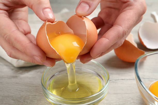 kobieta oddzielająca żółtko jaja od białego nad szklaną miską przy drewnianym stole, zbliżenie - eggs animal egg cracked egg yolk zdjęcia i obrazy z banku zdjęć